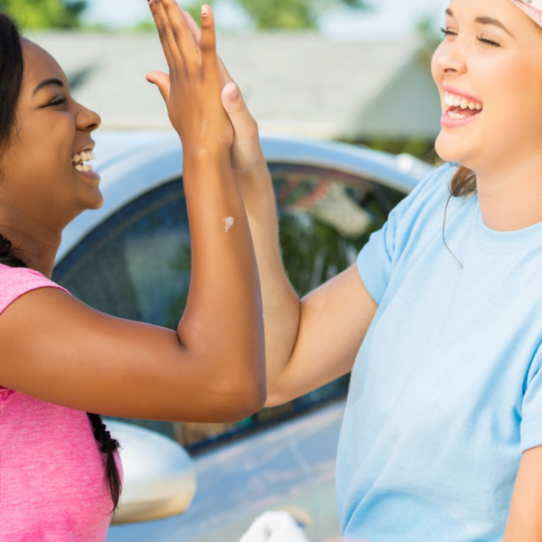 Two teenage girls high fiving while volunteering at a car wash.