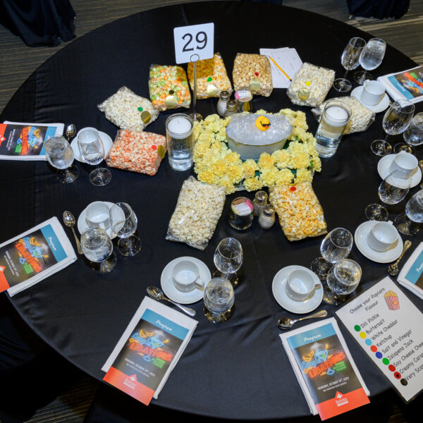 The table set up at the 2023 Laughs + Libations event. The table is complete with bags of flavored popcorn and the center piece which is short flowers with a bathtub on them with a duck floating on the bubbles.