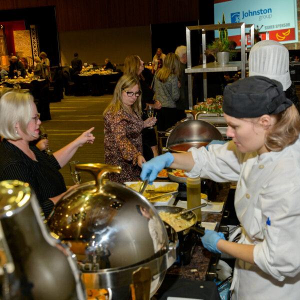 People being served at one of the food stations at the 2023 Laughs + Libations event.