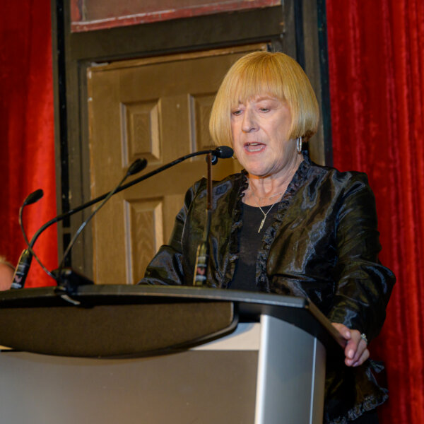 Cindy Stevens, Chair of the RHCF board gives a speech at the podium of the 2023 Laughs + Libations event.