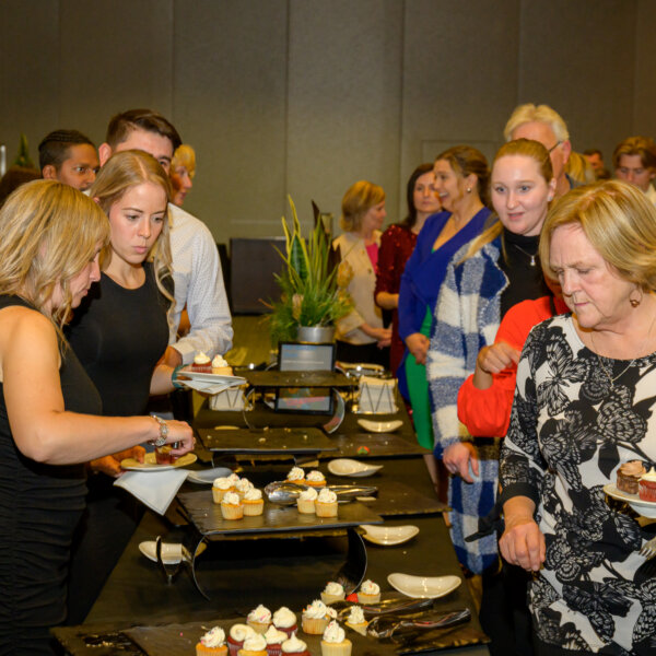 People lining up and serving themselves at the dessert table at the 2023 Laughs + Libations event.