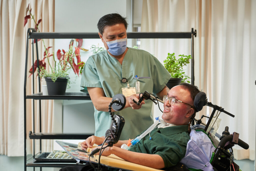 A male nurse helps a man in a wheelchair with his medical equipment.