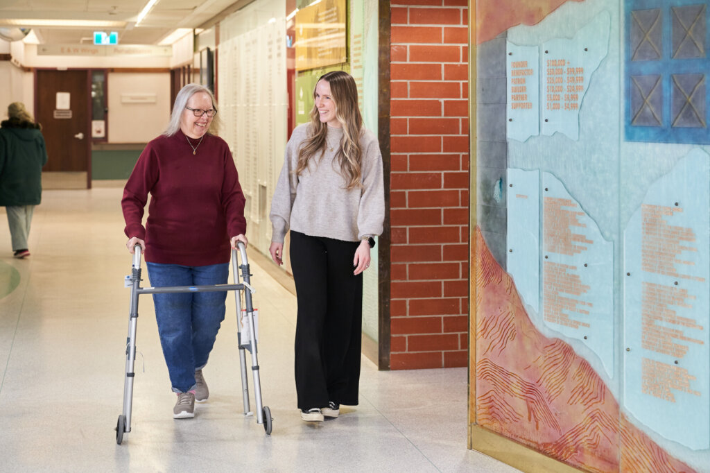 A Therapeutic Recreation Facilitator walks with a resident using a walker.