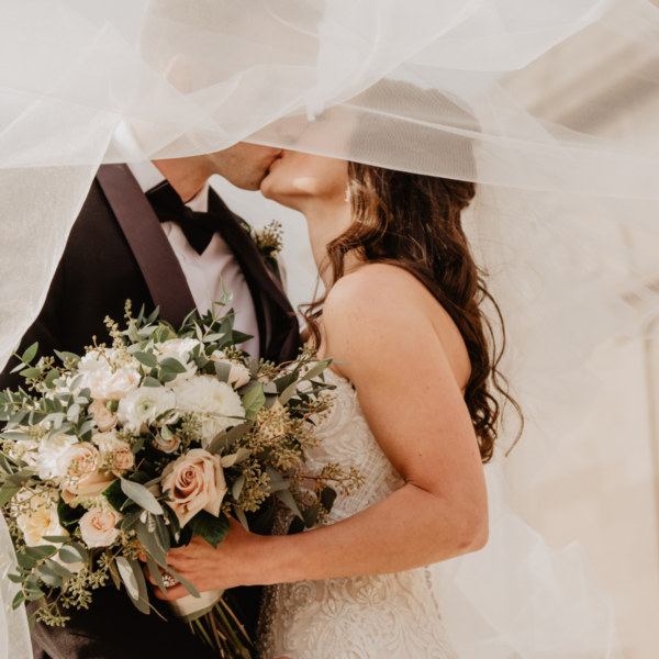 Photo of a bride holding flowers and kissing the groom.