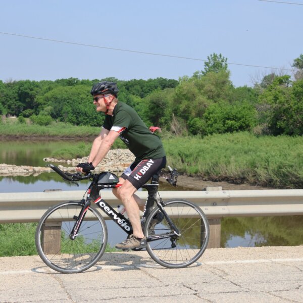 A cyclist smiling and riding over a bridge.