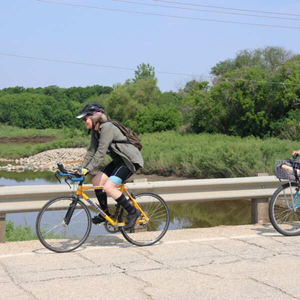 Two cyclists smiling and riding over a bridge.