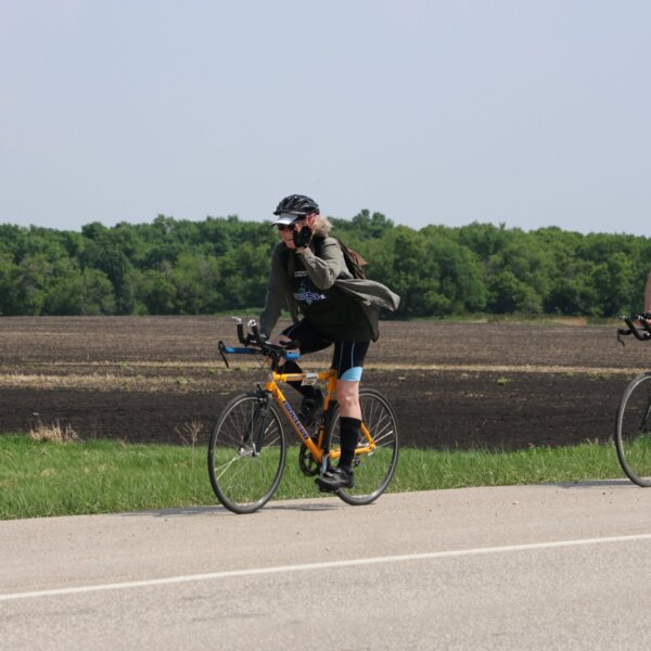 Two cyclists smiling and waving in front of a farmer's field.
