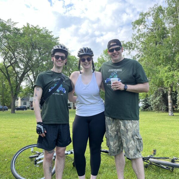 Three cyclists off of their bikes pose for a photo after completing their ride.