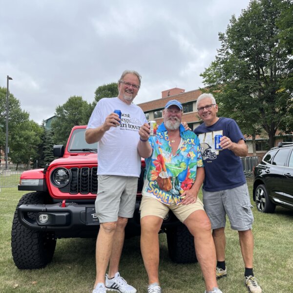Three men pose for a photo holding their drinks in front of a red Jeep from Birchwood.