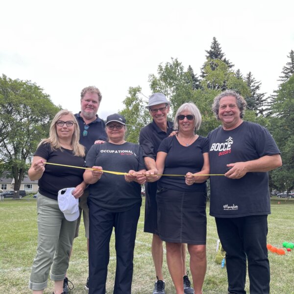 A bocce ball team of 6 poses with a measuring tape.