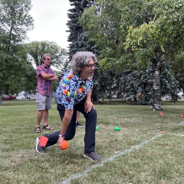 A man throws an orange ball as two others watch.