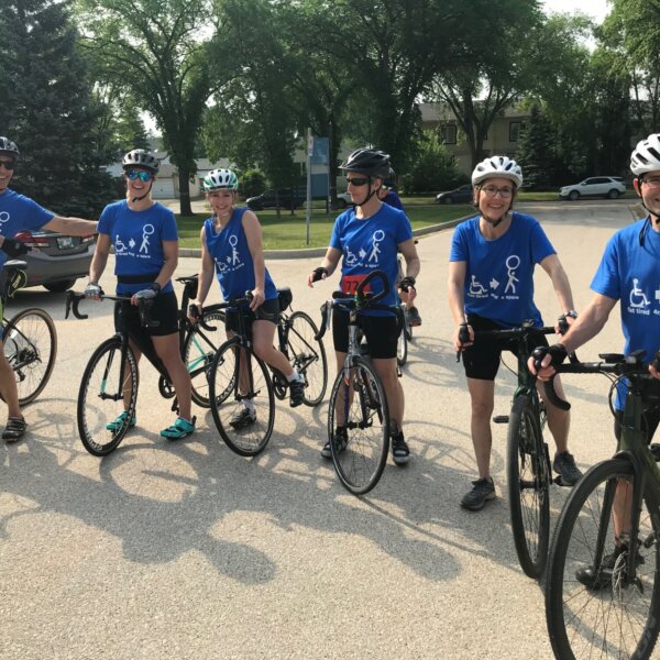 6 Cyclists smiling and posing for a photo wearing blue t shirts.