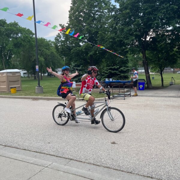 Two cyclists on a tandem bicycle celebrating as they finish their ride.