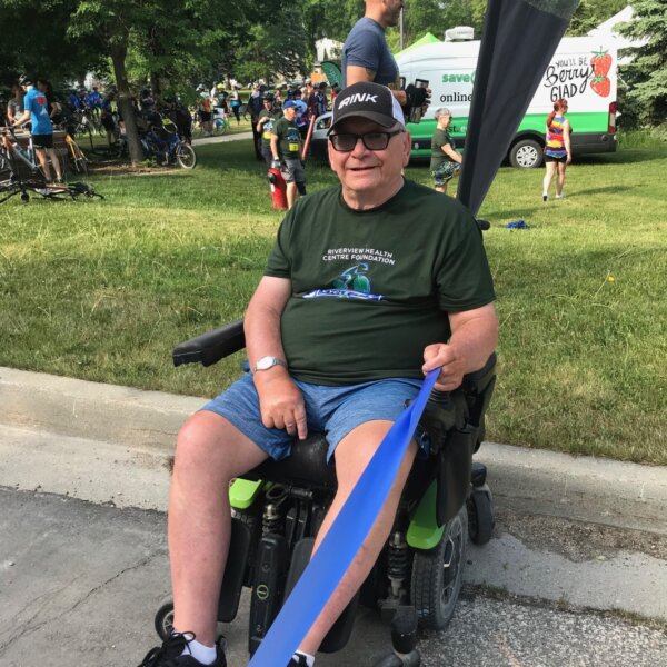 A resident in a wheelchair smiling for a photo as he holds half of the start line.