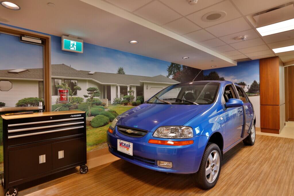 A blue chevy hatchback parked in the Alzheimer's Centre of Excellence. The car is stationary and can not be driven. 